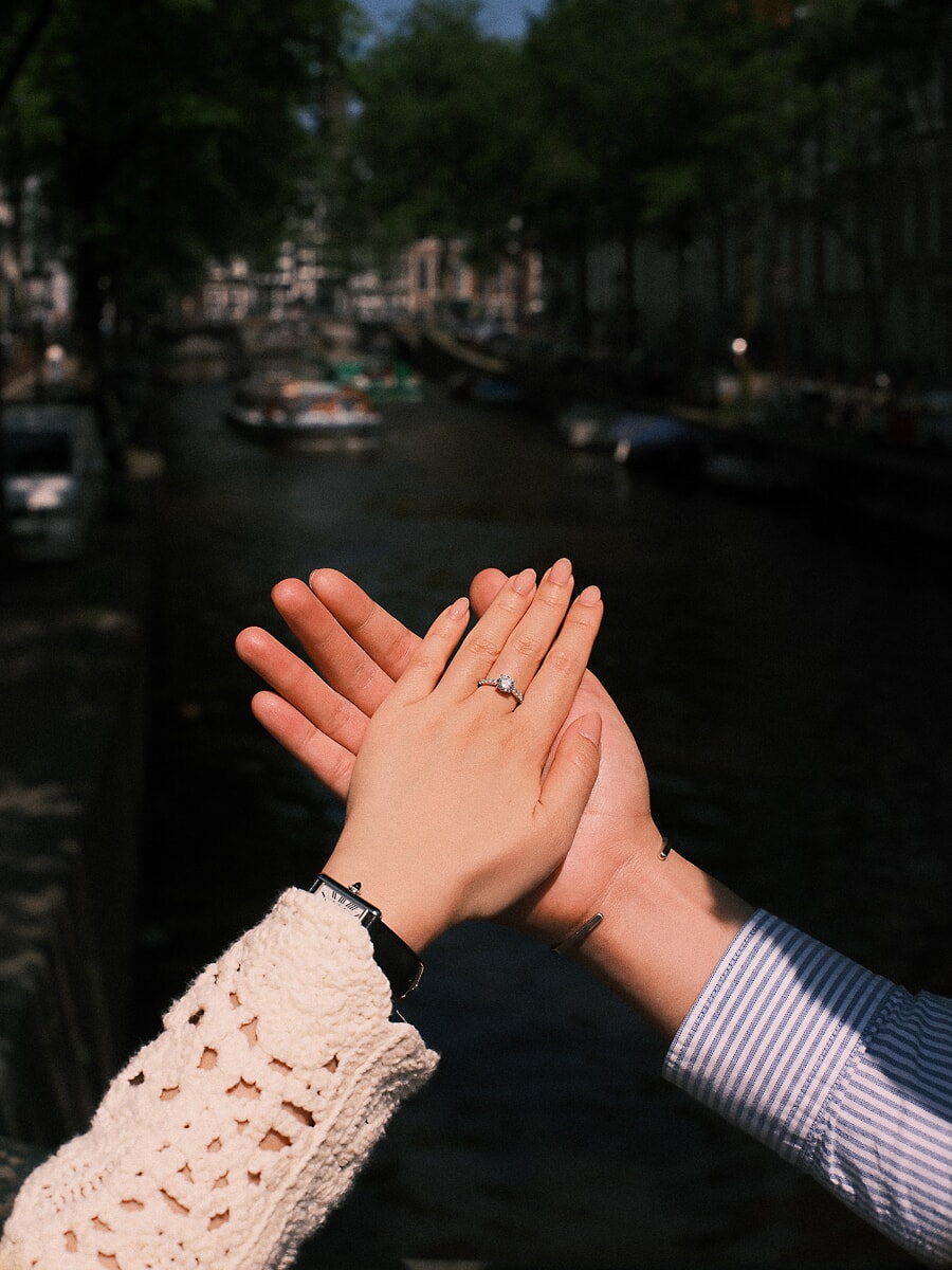 Engagement SP10 Verhalende close-up van handen die elkaar palm aan palm raken met de diamanten ring boven het water van een Amsterdamse gracht