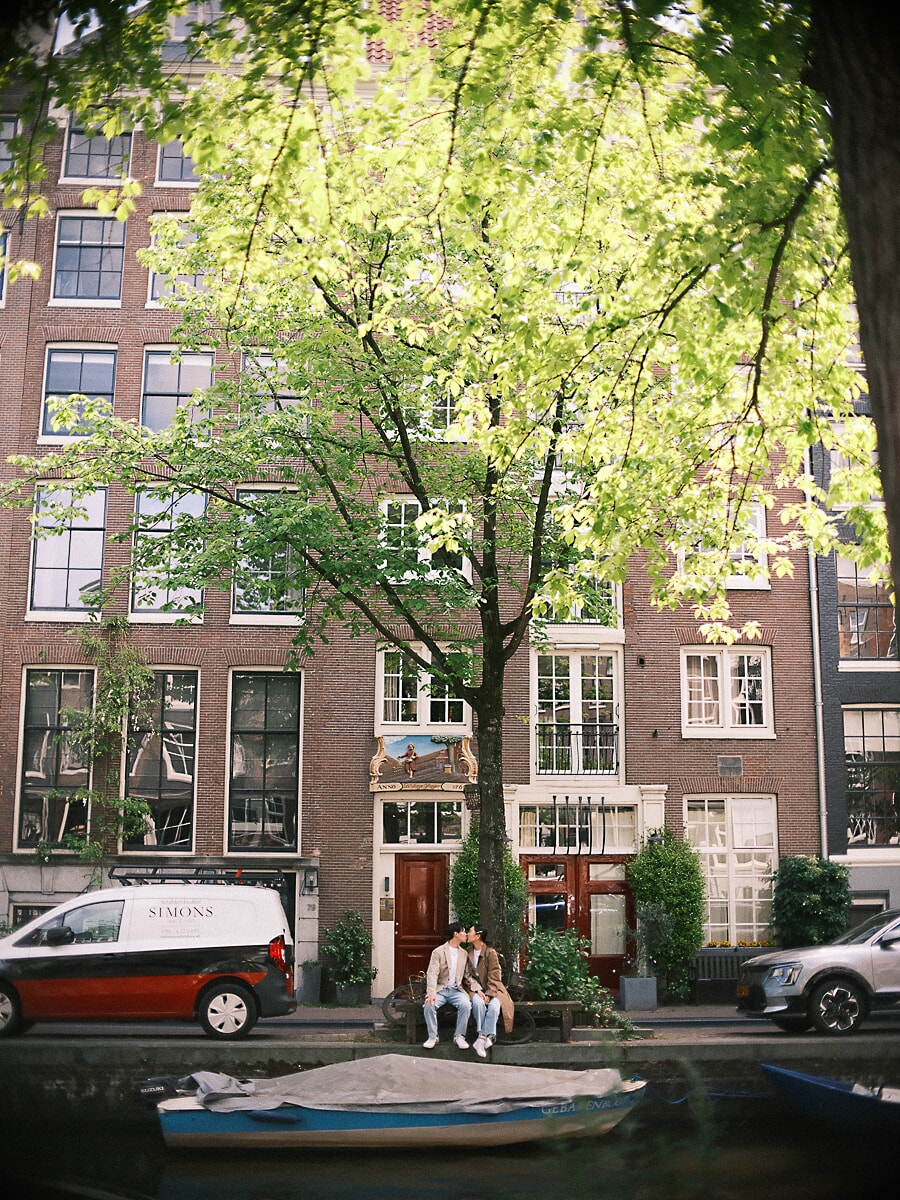 Loveshoot SP11 Documentair koppelportret van een stel dat elkaar kust op een bankje voor een hoog Amsterdams grachtenpand