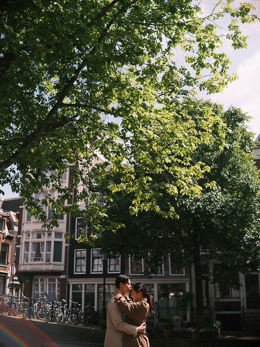 Loveshoot SP3 Romantisch stel kust elkaar onder een groene boom langs een Amsterdamse gracht met fietsen op de achtergrond