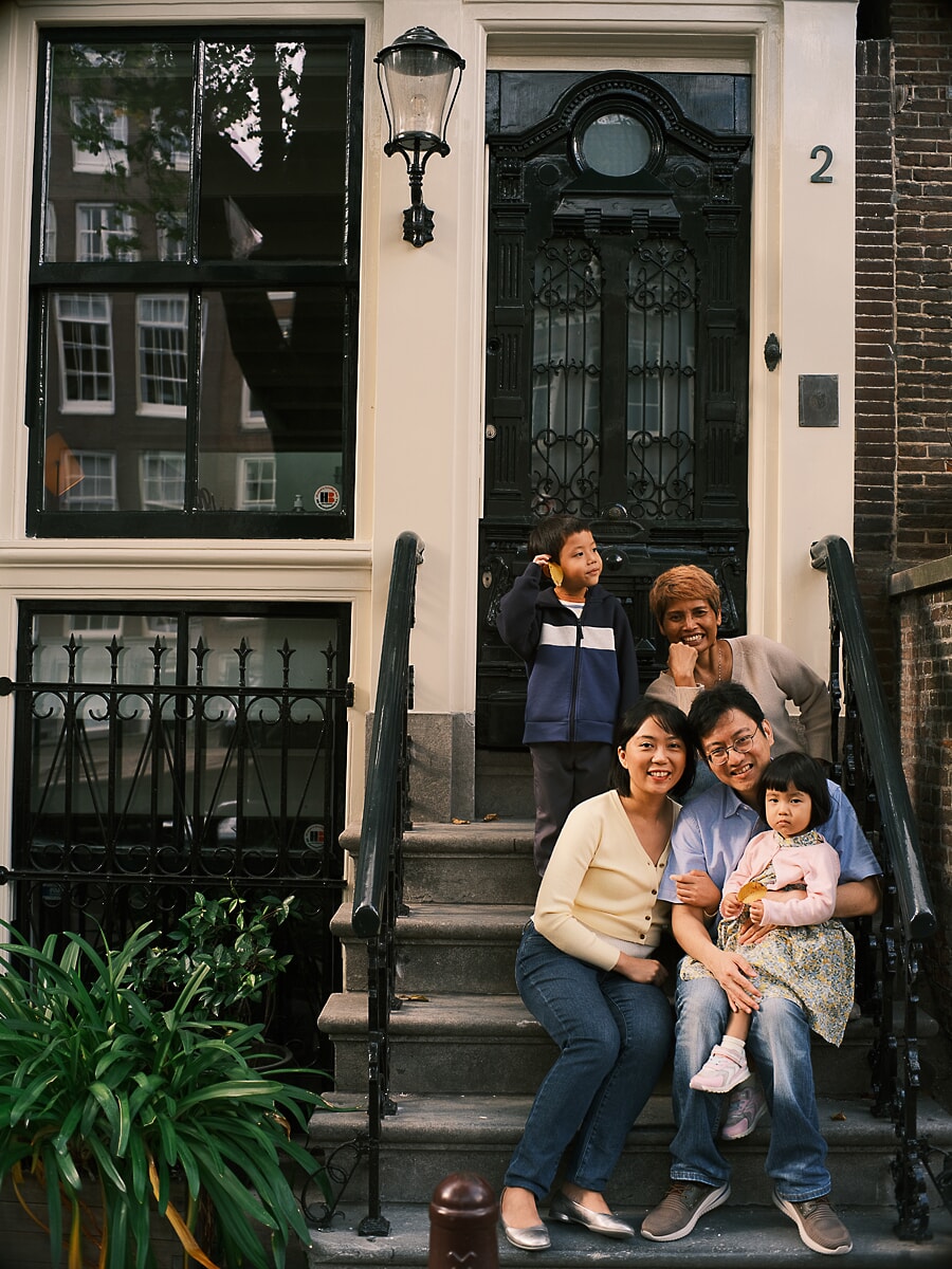 Family SP1 Op de stoep van een grachtenpand komen drie generaties samen, een oma lacht naast haar kleinkinderen, vastgelegd door een familiefotograaf in Amsterdam