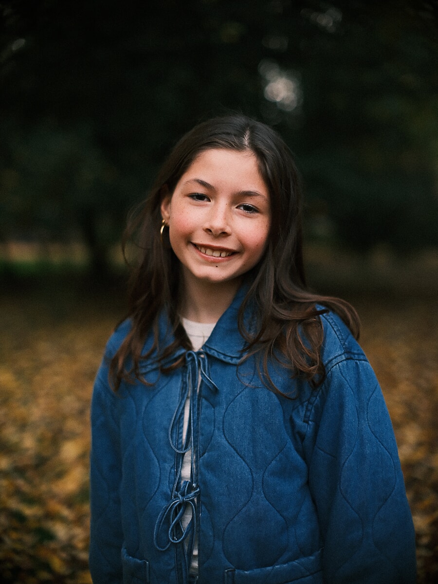 Family SP15 Ontspannen kinderportret van een lachend meisje in een spijkerjasje tussen de herfstbladeren in een Amsterdams park