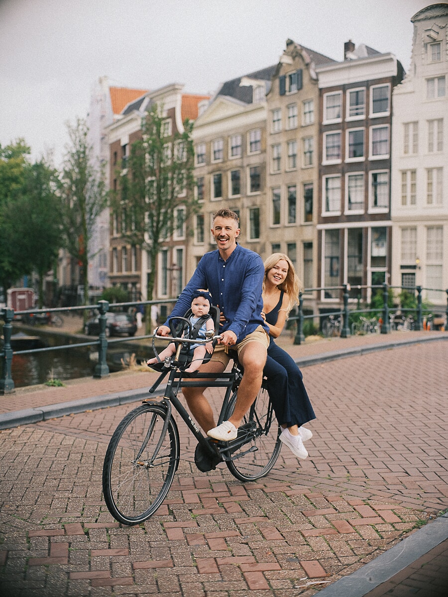 Family SP2 Zomerse gezinsfotoshoot terwijl ouders langs een Amsterdamse gracht fietsen met hun baby in een fietsstoeltje