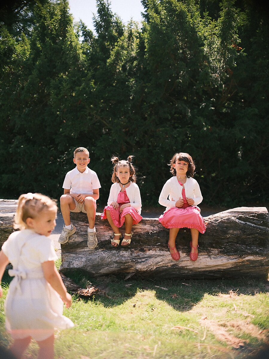 Family SP5 Vier kinderen in roze en wit op een omgevallen boomstam in een zonnige tuin, een speels moment vol familiefotografie