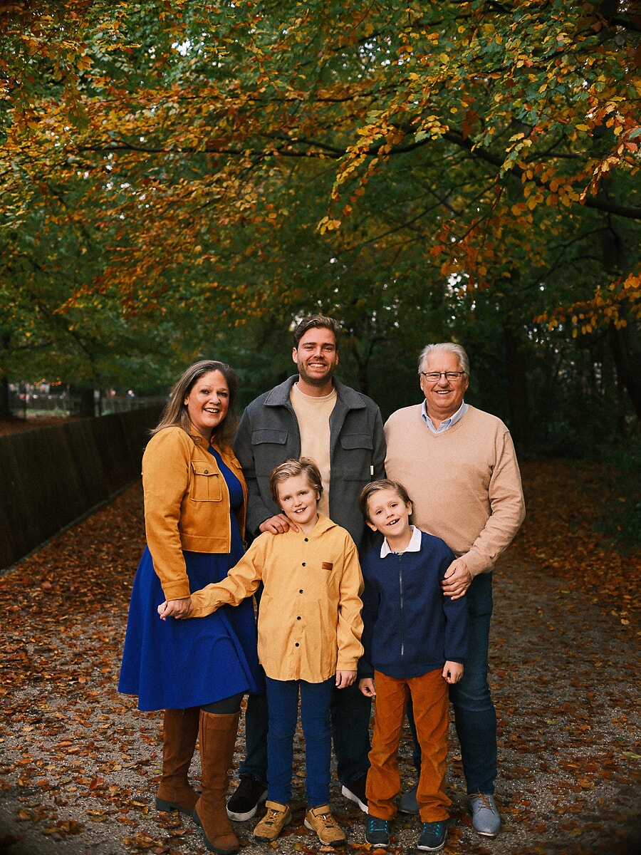 Family SP6 Een opa sluit aan bij de ouders en twee jongens op een met bladeren bedekt bospad, drie generaties samen voor hun familieportretten