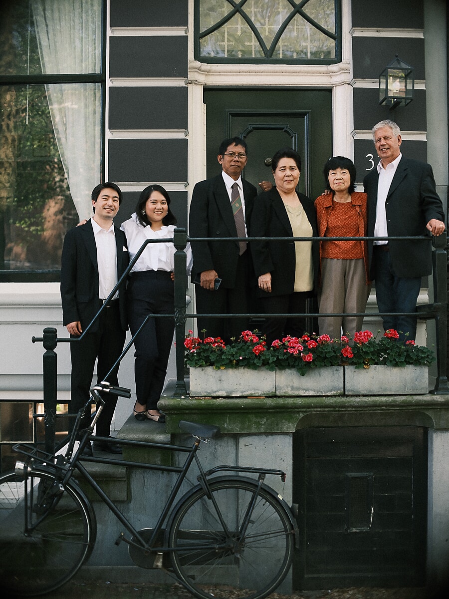 Group Family SP1 Formeel geklede familie van zes bij de deur van een grachtenpand voor een gouden jubileumportret, met een fiets tegen de stoep in Amsterdam
