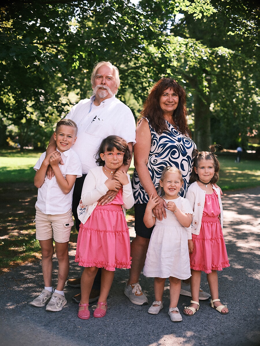 Group Family SP10 Familiefotograaf in Amsterdam legt grootouders met hun vier kleinkinderen vast in een zonnig park, de kinderen in roze en wit