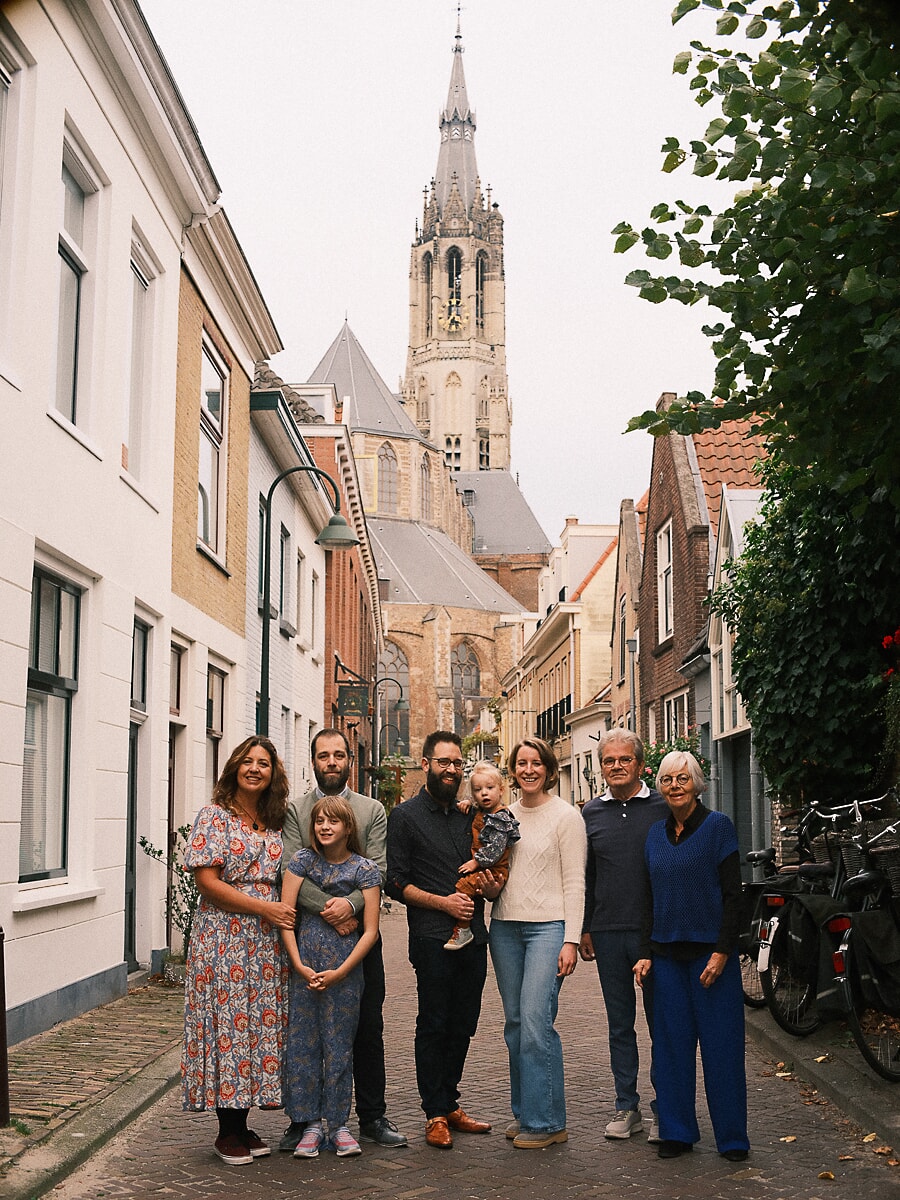 Group Family SP11 Uitgebreide familiereünie tijdens een fotoshoot in een geplaveide straat, met een hoge kerktoren op de achtergrond in herfstlicht