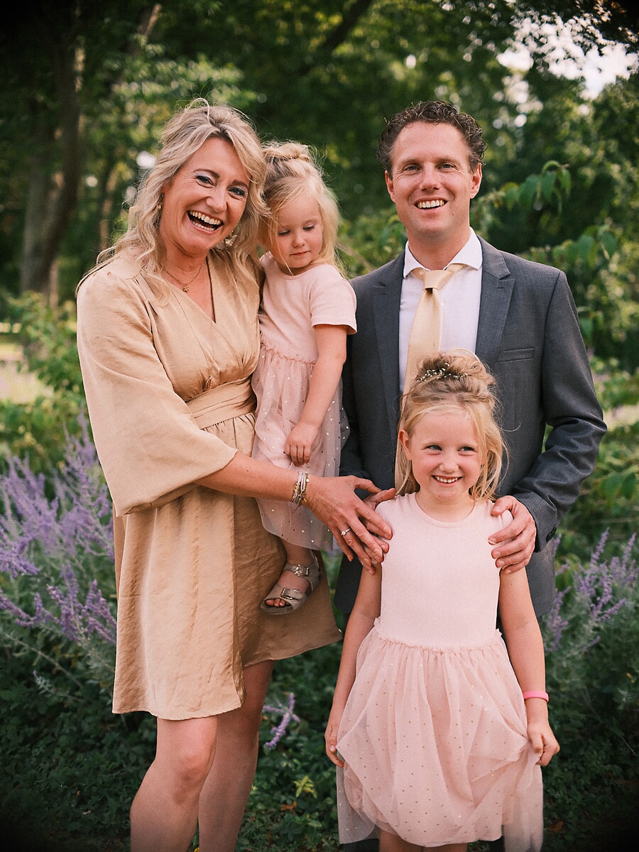 Group Family SP3 Ouders en hun twee dochters lachen samen tussen de lavendel in een groene tuin, de meisjes in zachtroze jurken, vastgelegd tijdens familiefotografie in Amsterdam