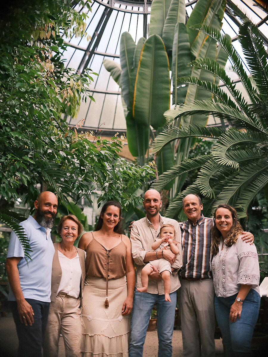 Group Family SP4 Expatgezin van drie generaties tussen het tropische groen in een botanische kas, met een baby in het midden tijdens hun familiefotografie sessie