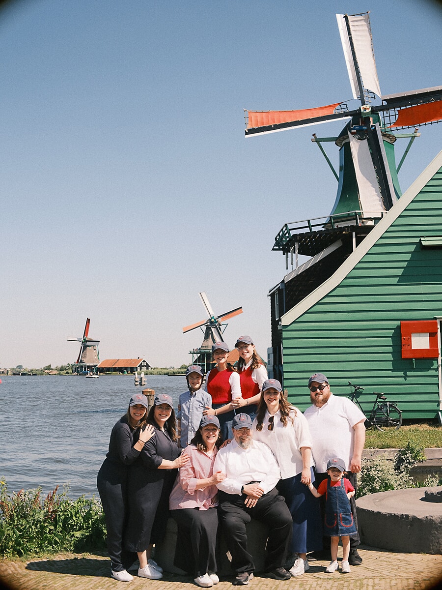 Group Family SP12 Grote familie met meerdere generaties in bijpassende petten bij het water aan de molens van de Zaanse Schans, drie generaties samen voor een familiereünie fotoshoot op een heldere zomerdag