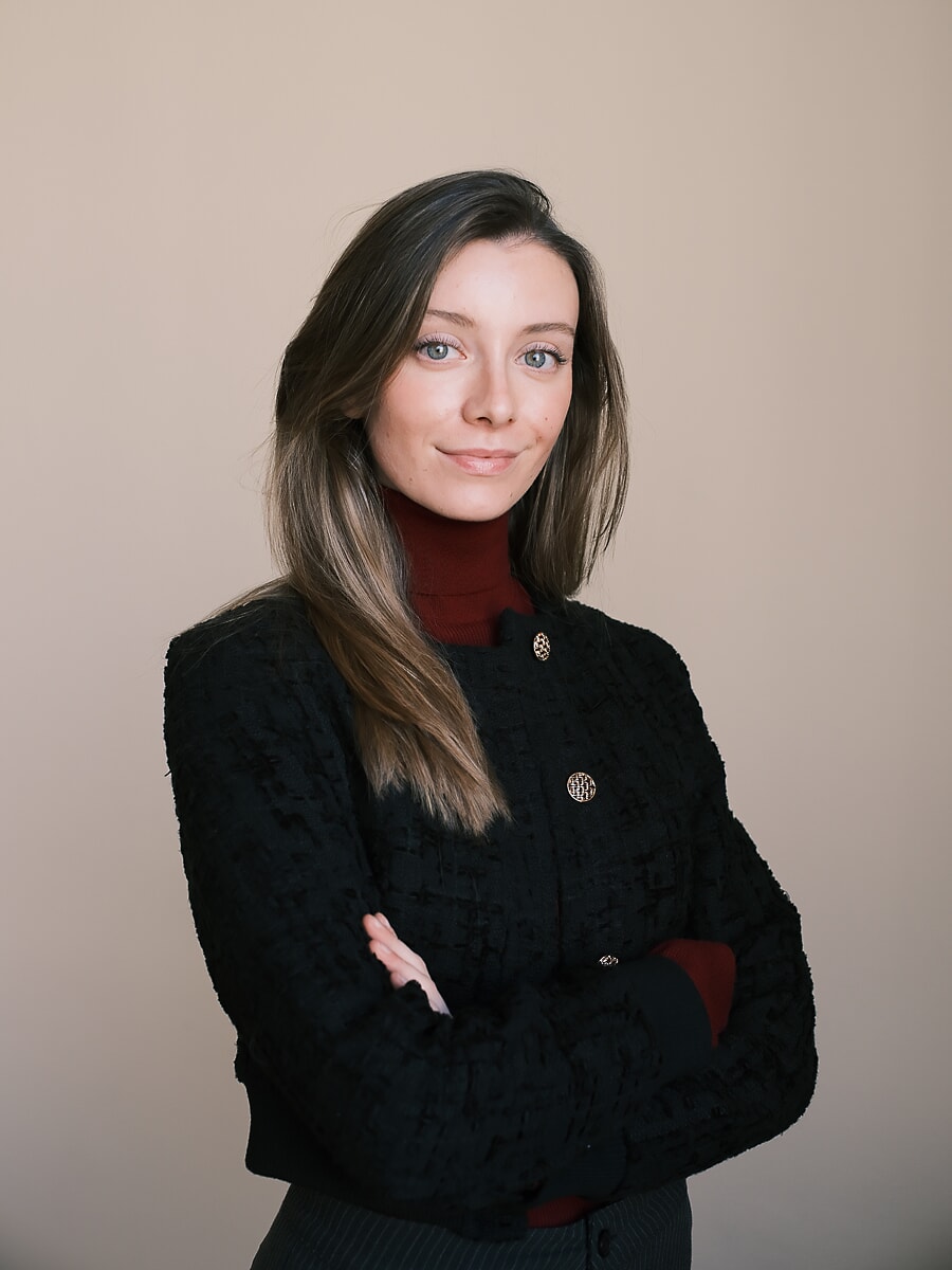 Vrouw in een zwart tweed jasje over een bordeauxrode coltrui met over elkaar geslagen armen, een zakelijk portret in Amsterdam