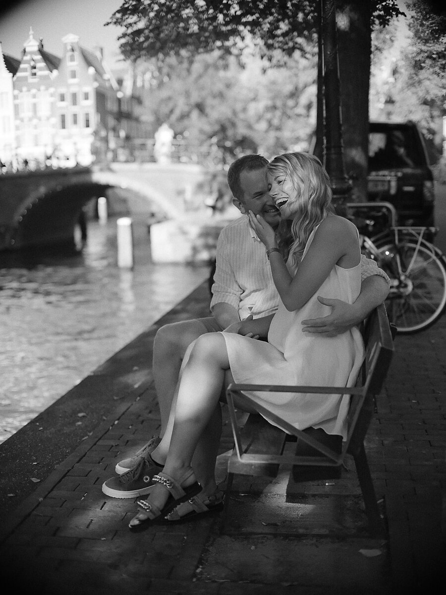 Lachend stel op een bankje langs de gracht, een zwart-wit beeld uit hun fotosessie