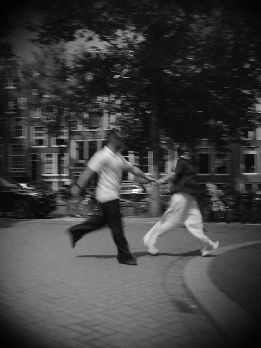 Zwart-wit bewegingsonscherpte van een stel dat hand in hand door de stad rent, spontaan en ongeposeerd