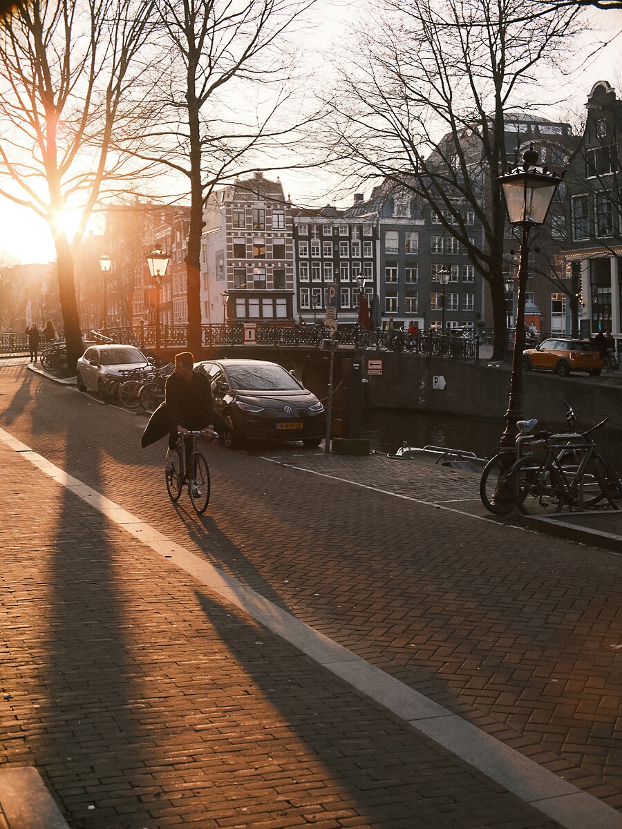 Fietser rijdt langs een Amsterdamse gracht in laag winterlicht, met lange boomschaduwen, een breed beeld uit de portretfotoshoot