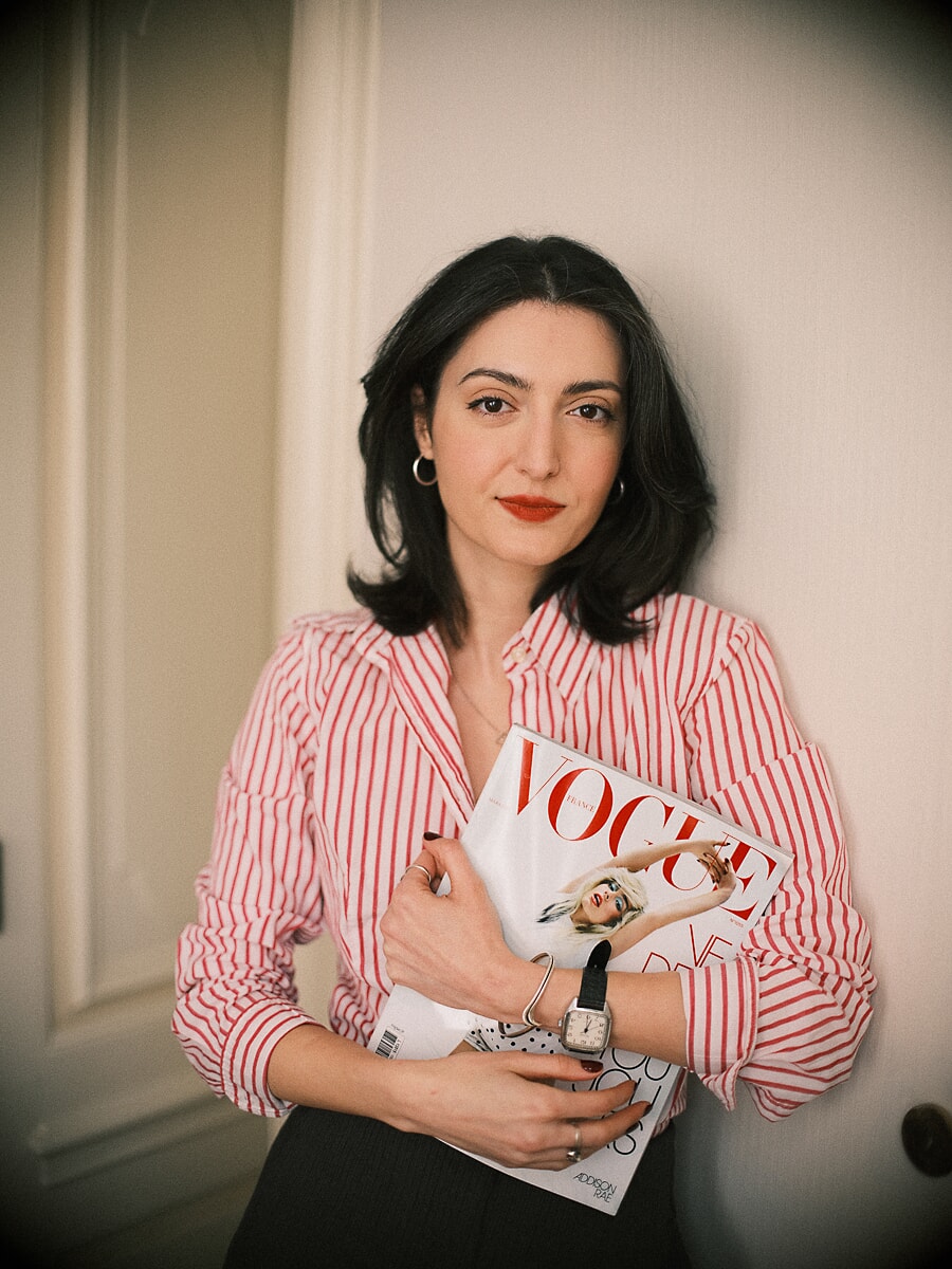 Redacteur in een roodgestreept overhemd houdt een stapel modetijdschriften vast tegen een crèmekleurige lambrisering, een brandingshoot in Amsterdam