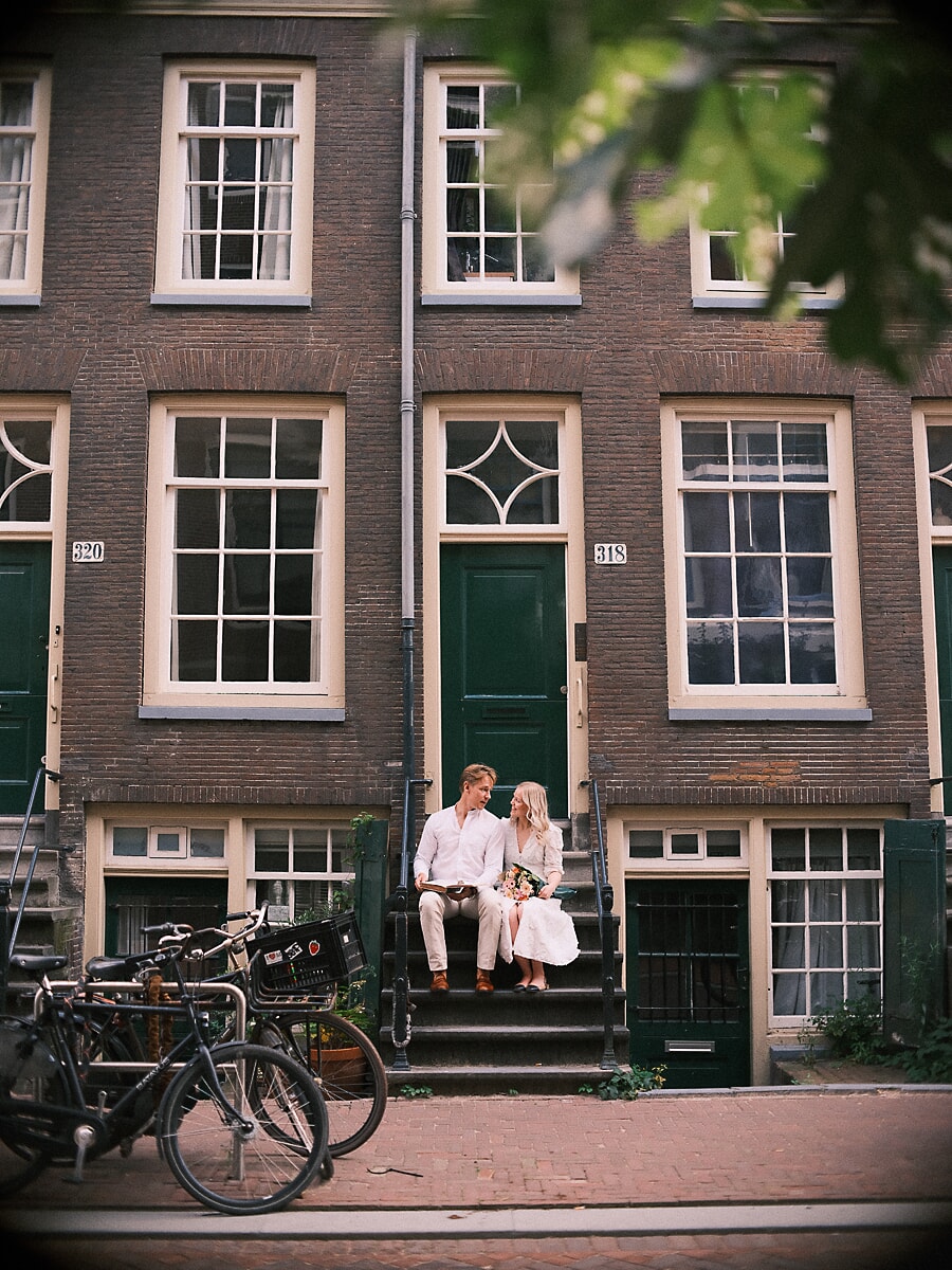 Verloofd stel op de stoep van een Amsterdams grachtenpand tijdens hun verlovingsfotoshoot, met fietsen langs de straat
