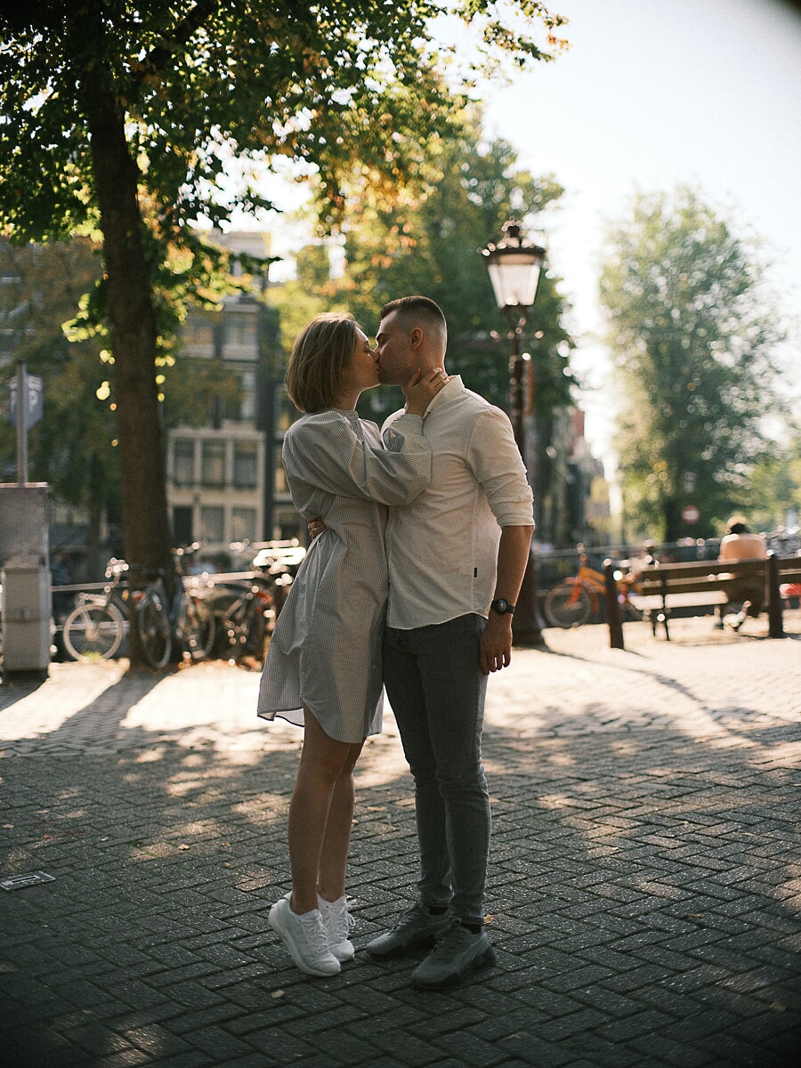 Verloofd stel kust op een zonnig plein tijdens hun verlovingsfotoshoot in Amsterdam