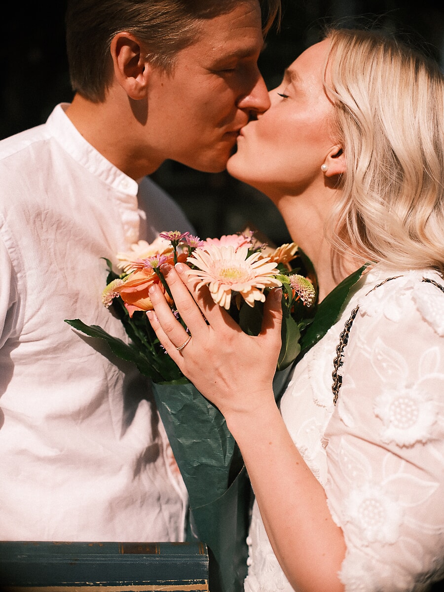 Verloofd stel kust boven een boeket gerbera's, haar verlovingsring zichtbaar op de stelen tijdens een pre-wedding fotosessie