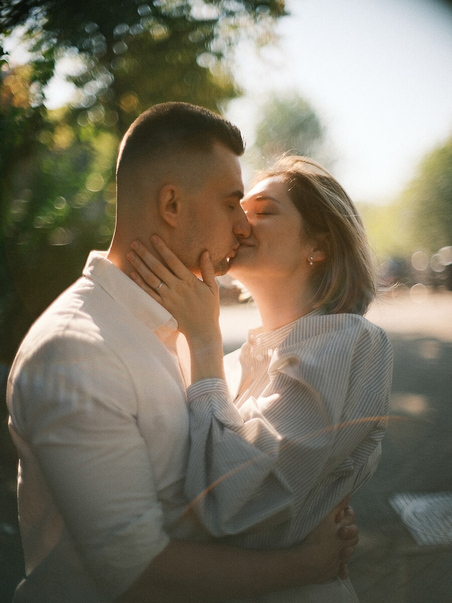 Verloofd stel kust in warm tegenlicht tijdens een romantische fotoshoot in Amsterdam, haar verlovingsring tegen zijn kaak