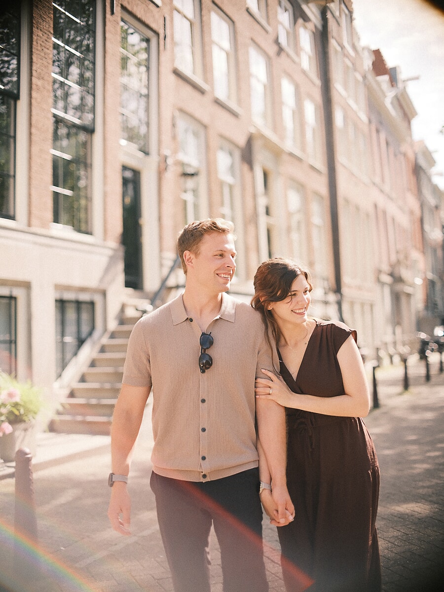 Verloofd stel wandelt arm in arm langs een gracht tijdens hun verlovingsfotoshoot, met zachte lensgloed