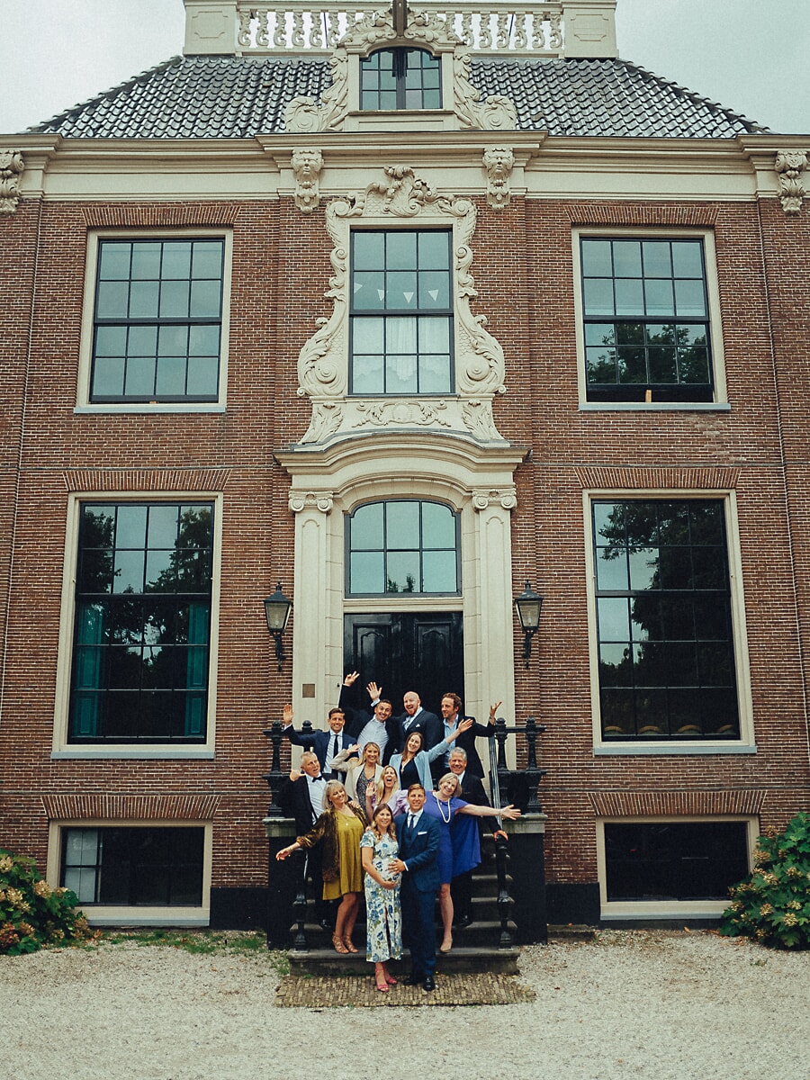 Group Family SP14 Uitgebreide familie zwaait vanaf de stoep van een groot Hollands landhuis, een uitbundige fotosessie met meerdere generaties voor de sierlijke bakstenen gevel