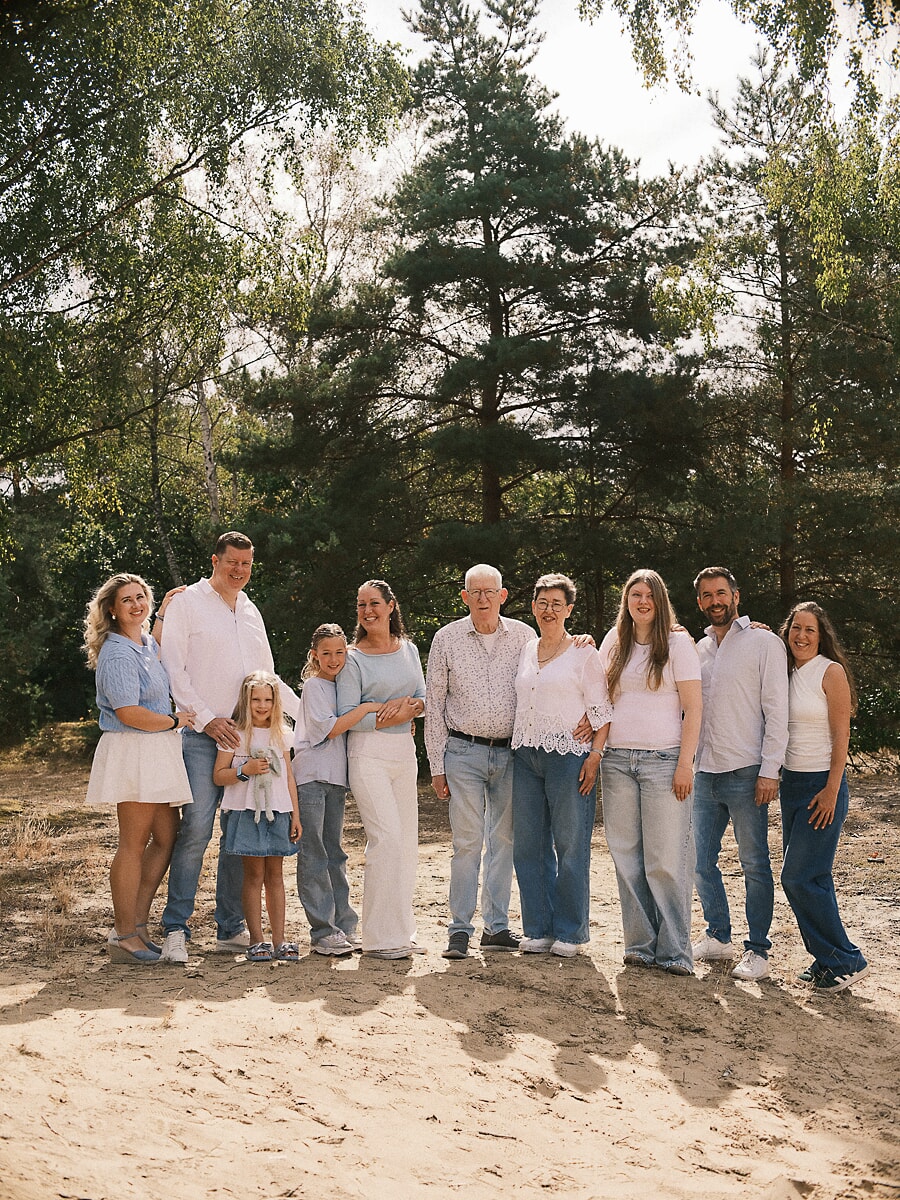 Tien familieleden in blauw en wit samen op het zand in een Nederlands bos, de grootouders in het midden