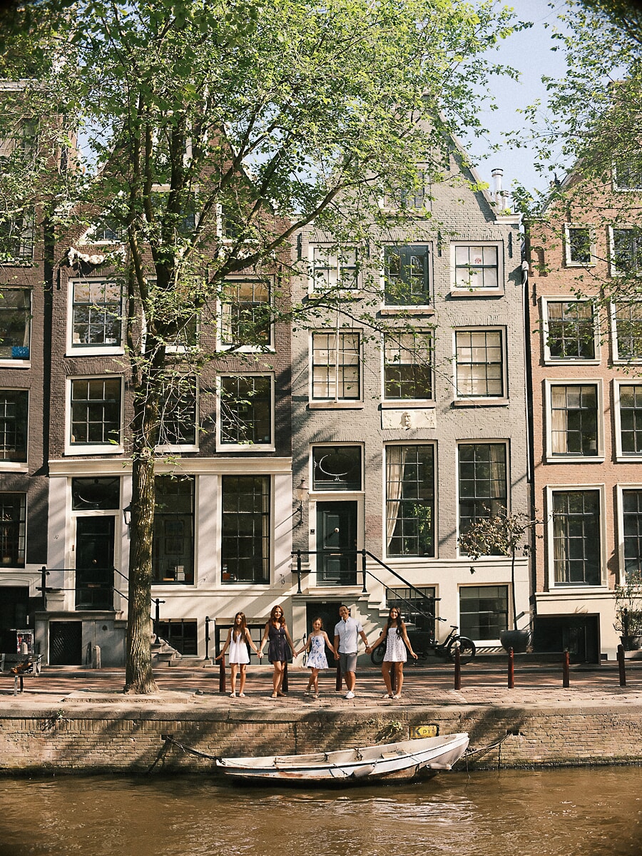Hand in hand langs de kade, een gezin van vijf klein onder de hoge Amsterdamse grachtenpanden