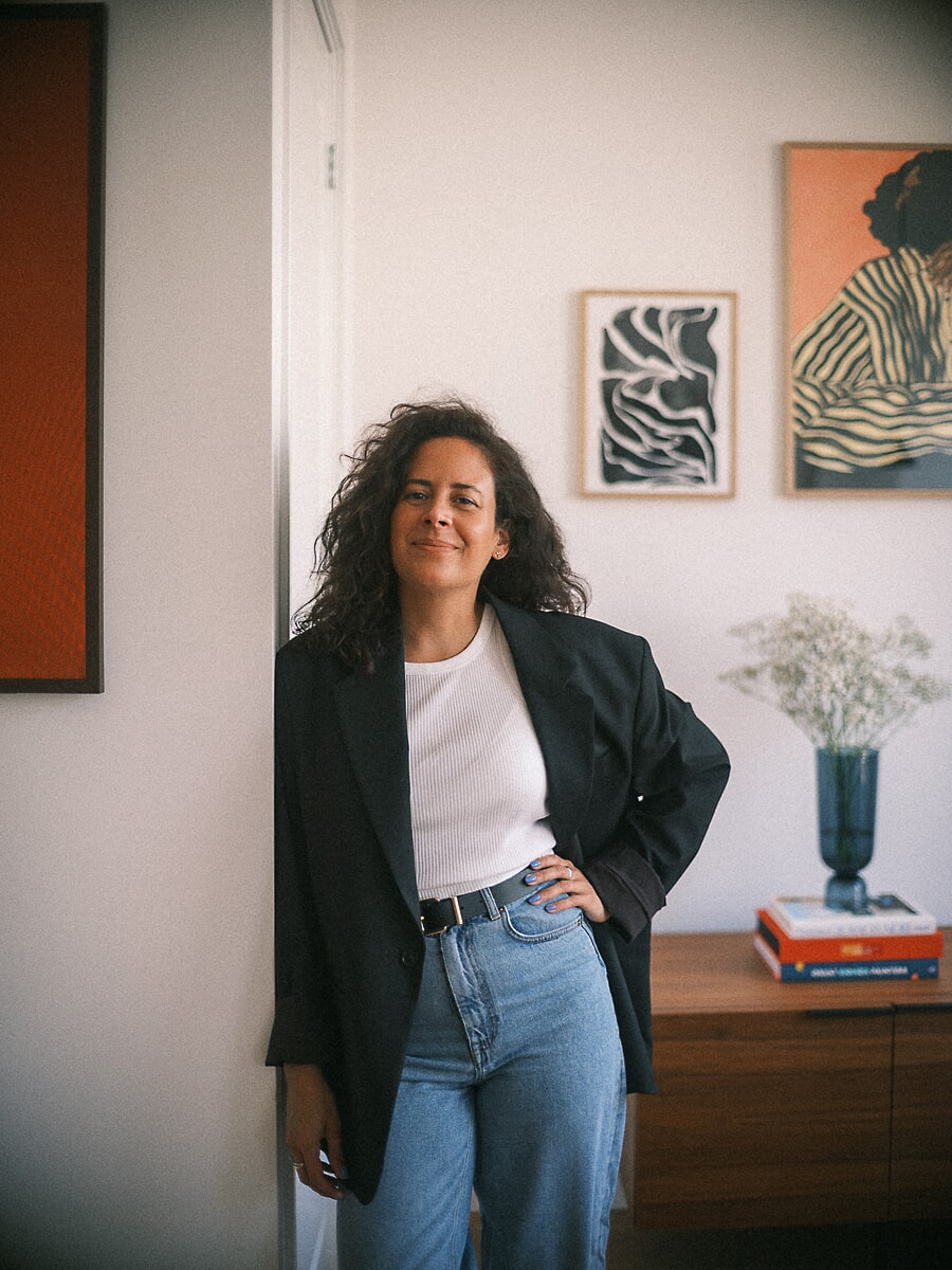Oprichter in een oversized blazer leunt in een deuropening, ingelijste prints en een dressoir achter haar, brandingfotografie in Amsterdam