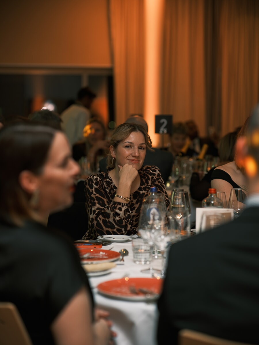 Gast in luipaardprint met haar kin op haar hand aan de dinertafel, warm licht achter haar, een bedrijfsevenement in Amsterdam