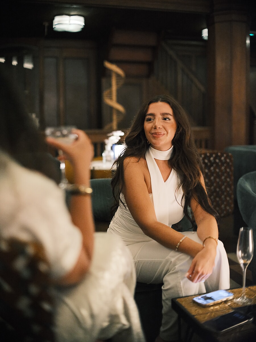 Gast in een witte jumpsuit lacht in een lounge met houten lambrisering en groenfluwelen banken, een bedrijfsevenement in Amsterdam