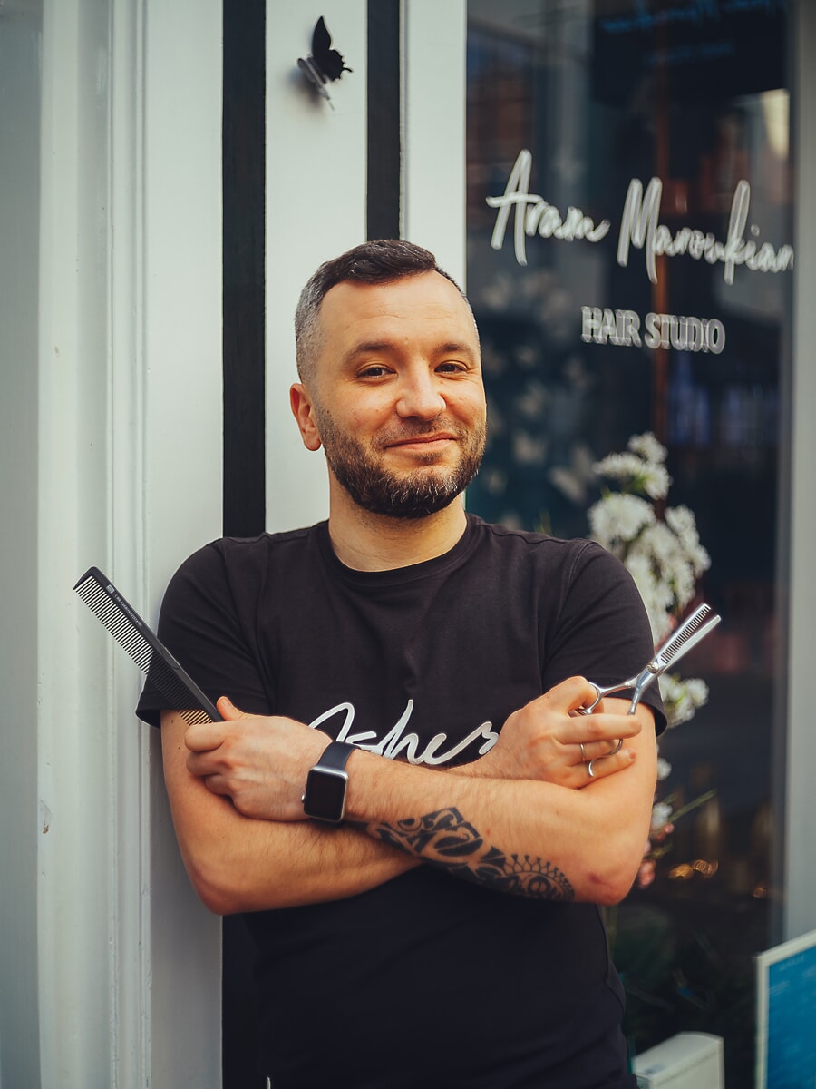 Kapper met een kam en schaar voor zijn borst gekruist, bij het raam van een salon