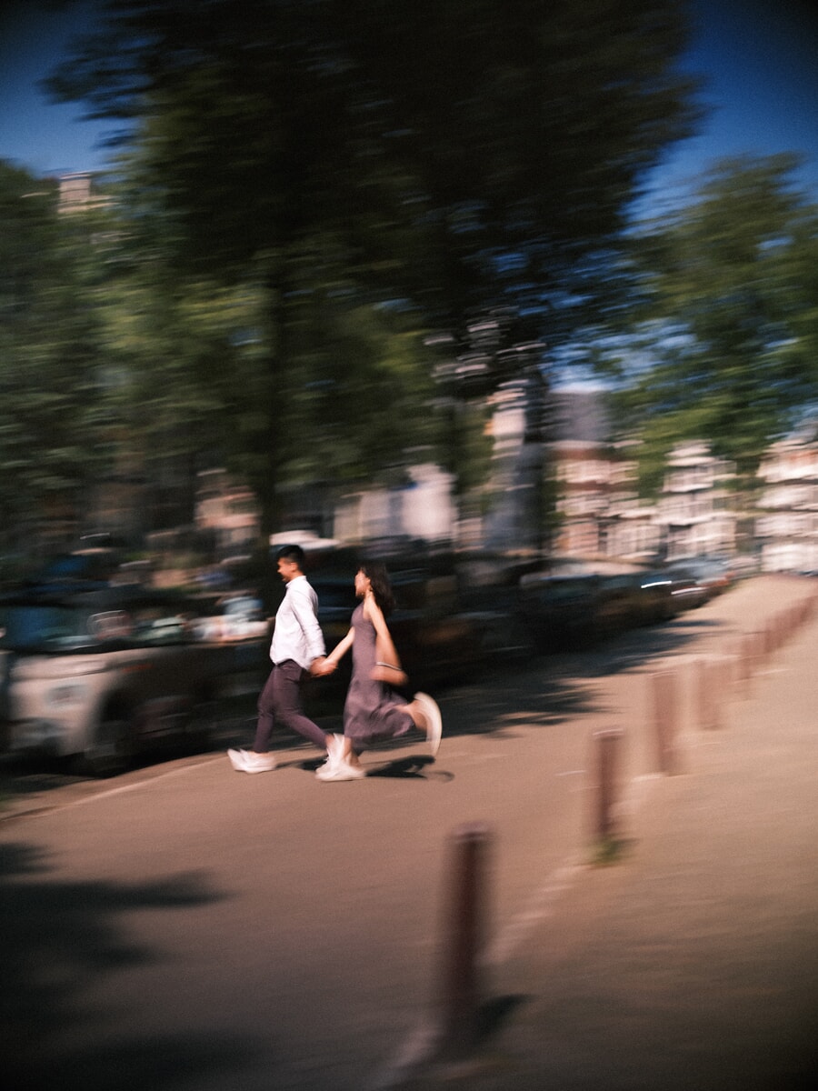Stel rent hand in hand door een straat langs de gracht in Amsterdam, met bewegingsonscherpte