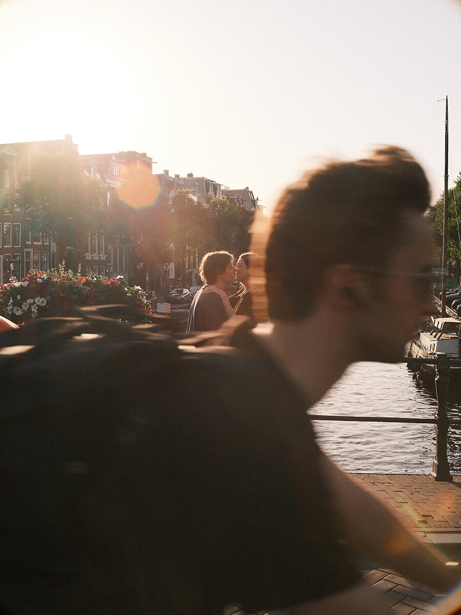 Stel kust bij zonsondergang terwijl een fietser vervaagd voorbijrijdt, documentaire koppelfotografie in Amsterdam