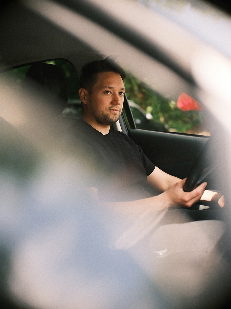 Man achter het stuur van een auto, gezien door het raamkozijn, met de voorgrond wegvallend in onscherpte