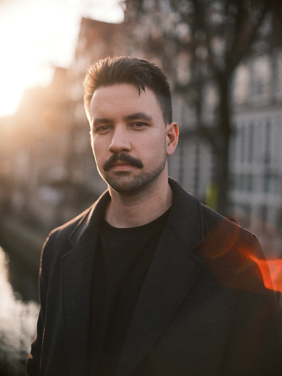 Close-upportret van een man in zwarte jas, met de oranje gloed en flare van een artistieke lens door het beeld