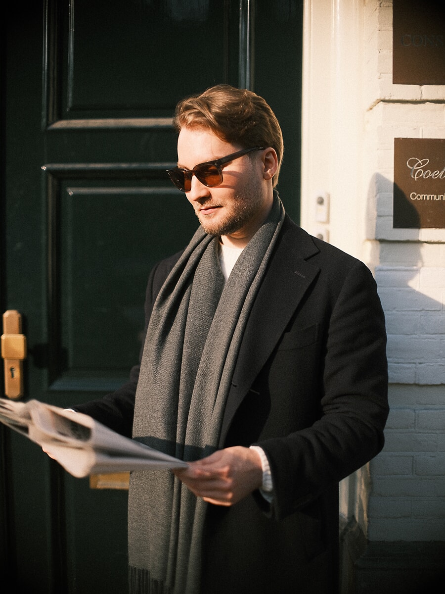 Man met zonnebril leest de krant voor een donkergroene deur in laag winterlicht, een spontane datingfoto