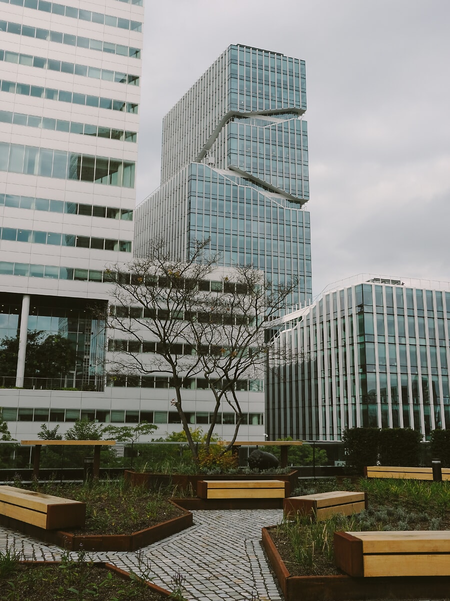 Gestapelde glazen kantoortoren boven een dakterras met houten banken en geplaveide paden, commerciële vastgoedfotografie in Amsterdam