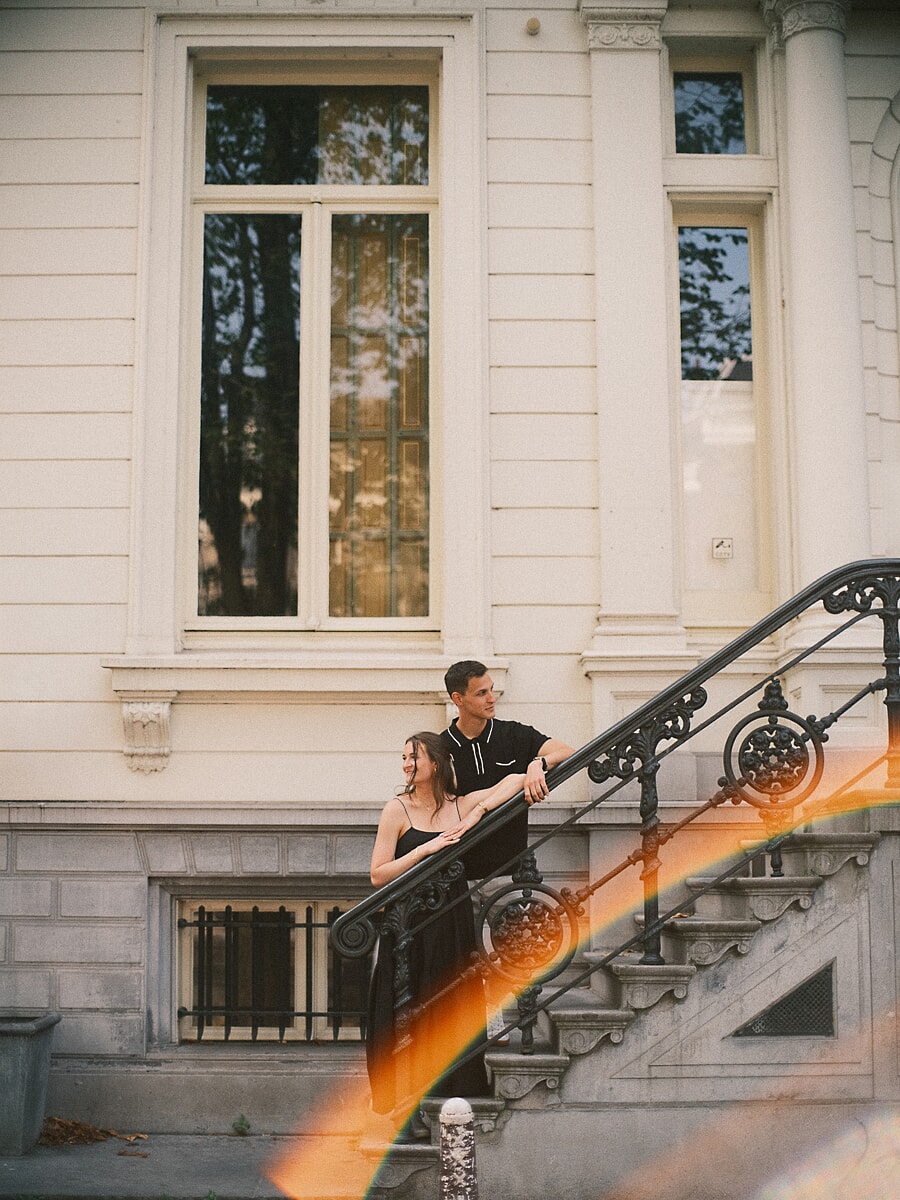 Pre-wedding koppelportret op de sierlijke trap van een Amsterdams grachtenpand, met filmische lensflare door het beeld