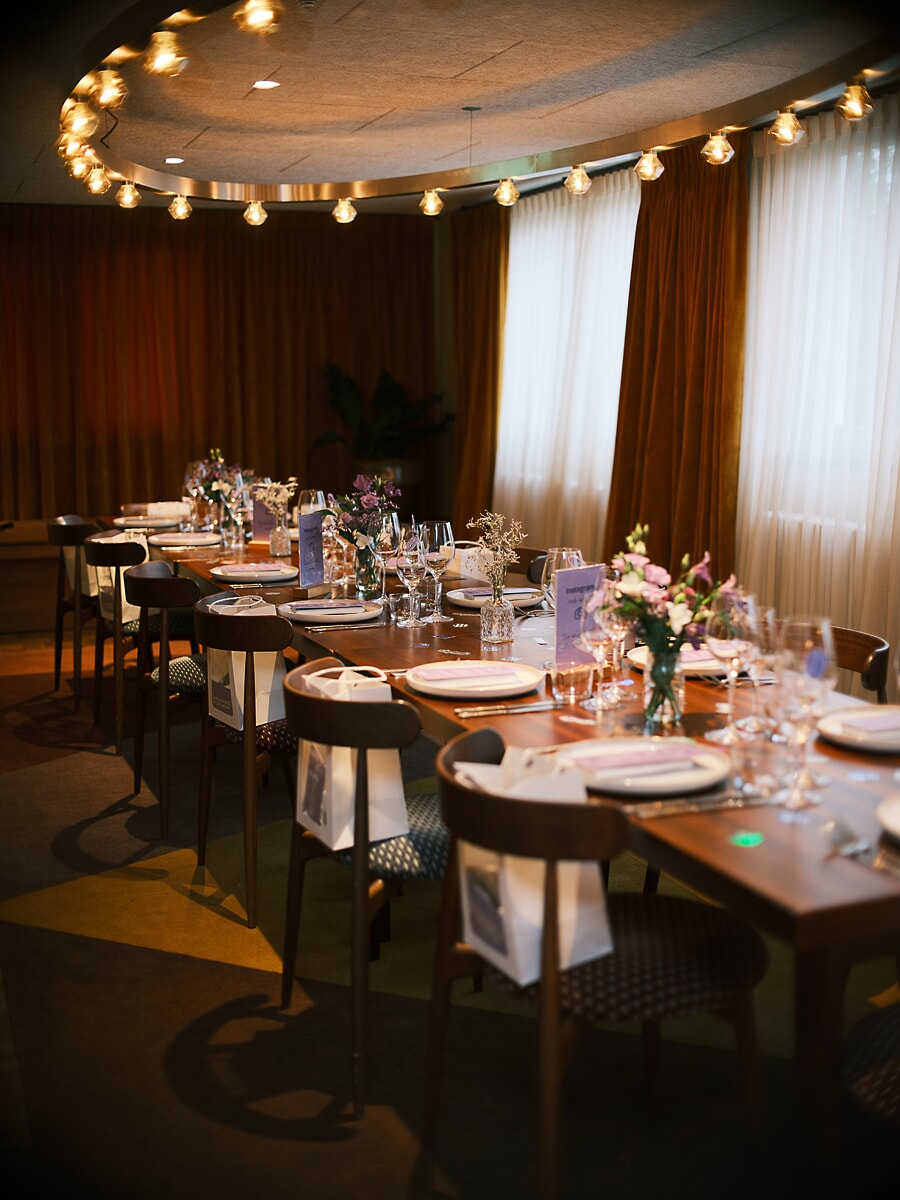 Lange tafel gedekt onder een ring van kale peertjes, met menukaarten en tasjes op elke plek, een zakelijk diner in Amsterdam