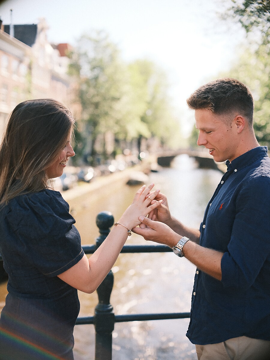 Man schuift de verlovingsring om haar vinger naast een heldere gracht, vlak na het huwelijksaanzoek in Amsterdam
