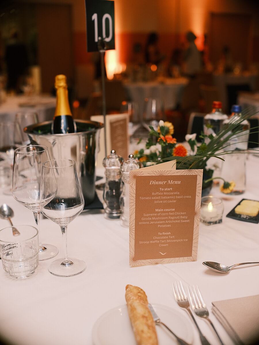 Tafeldetail met de menukaart van het diner, champagne in een ijsemmer en een laag bloemstuk