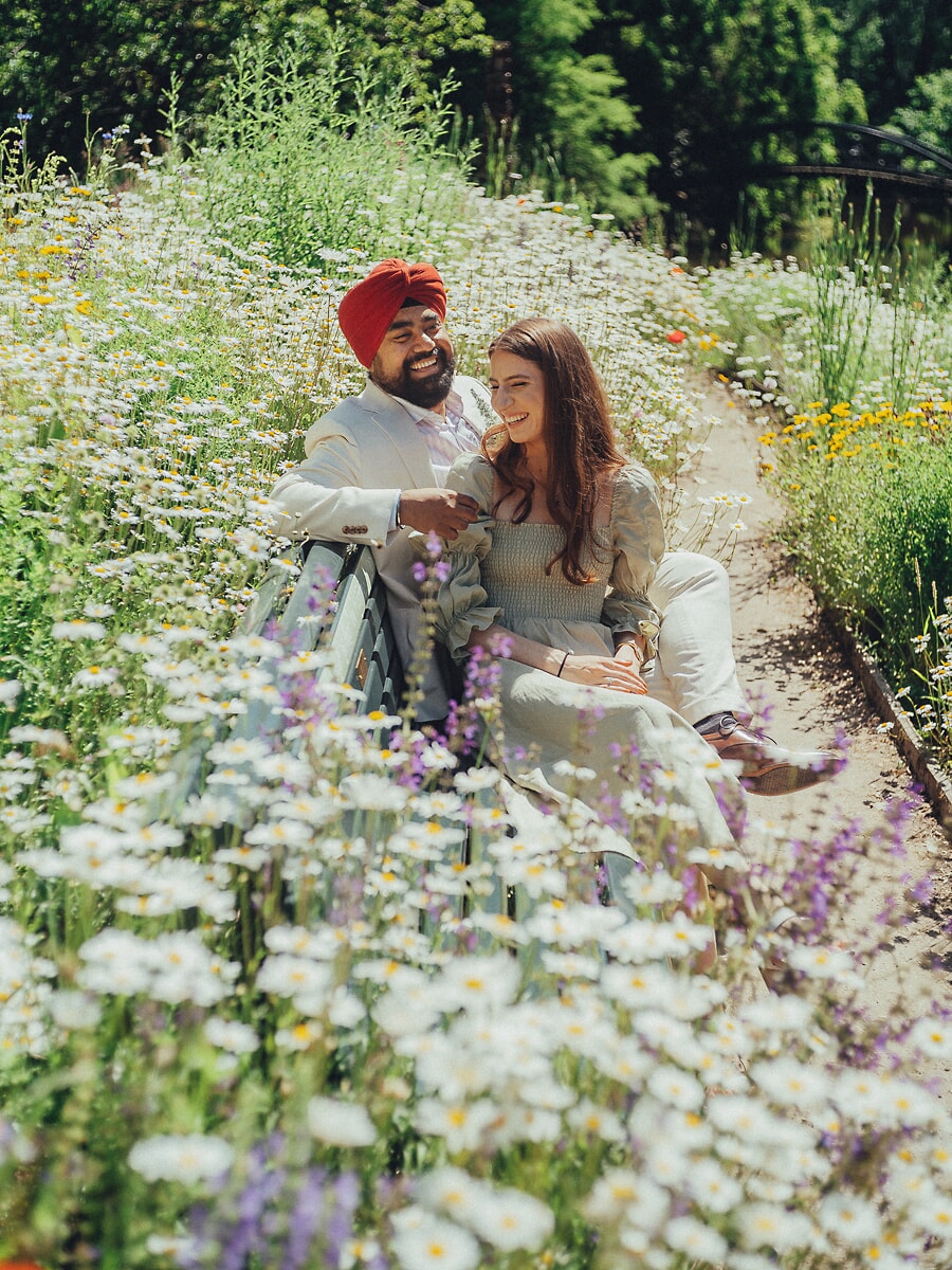 Wedding Ceremony SP16 Dicht bij elkaar op een bankje tussen madeliefjes in een zonnige tuin ontspant het stel voor een trouwfotograaf in Amsterdam