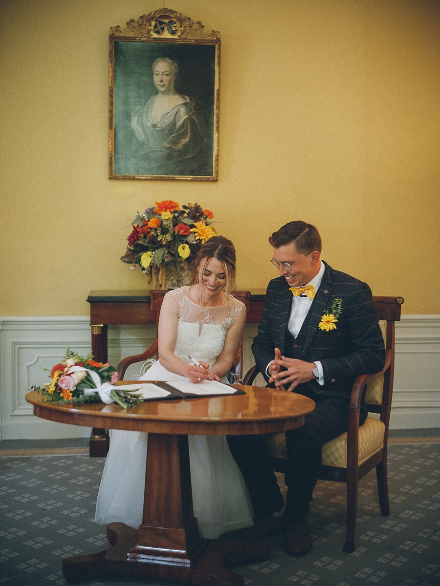 Wedding Ceremony SP22 Bruid ondertekent de trouwakte naast haar bruidegom, een herfstboeket ernaast, gefotografeerd door een trouwfotograaf in Amsterdam
