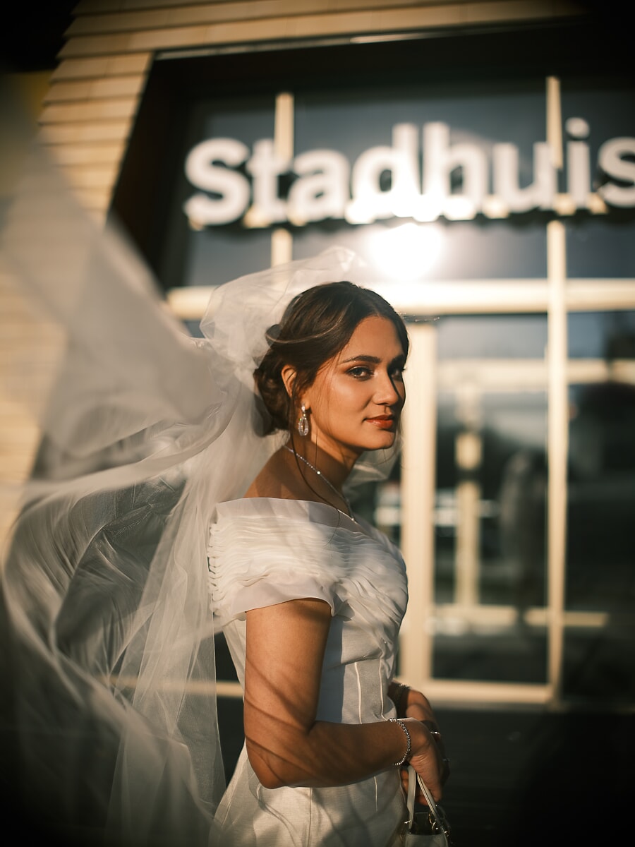 Wedding Ceremony SP3 Bruid met sluier staat even stil voor een Amsterdams stadhuis tijdens het gouden uur, een cinematisch bruidsportret