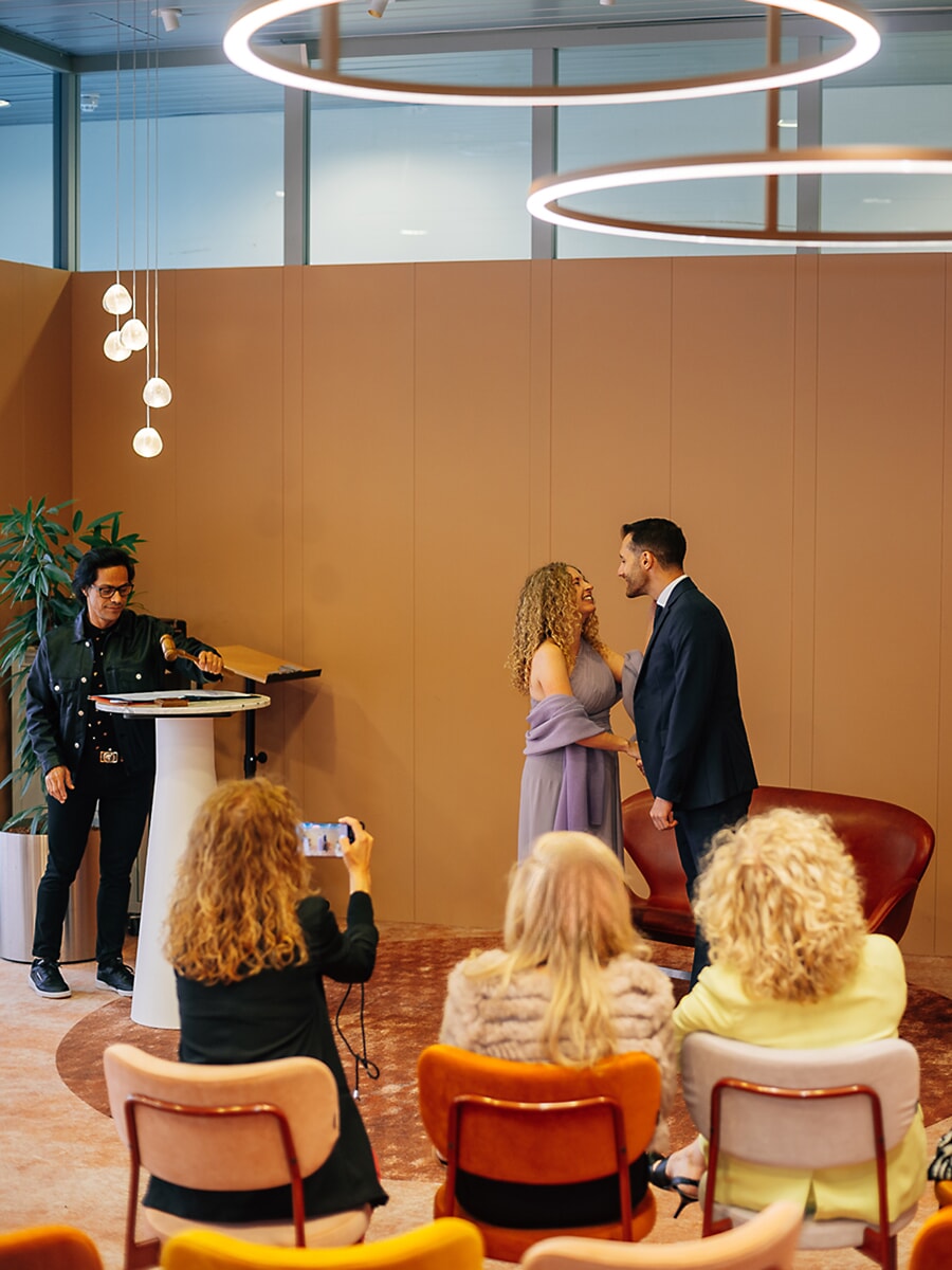 Wedding Ceremony SP32 Stel spreekt de geloften uit in een moderne locatie met ronde hanglampen, gasten kijken toe, een spontaan beeld van een trouwfotograaf in Amsterdam