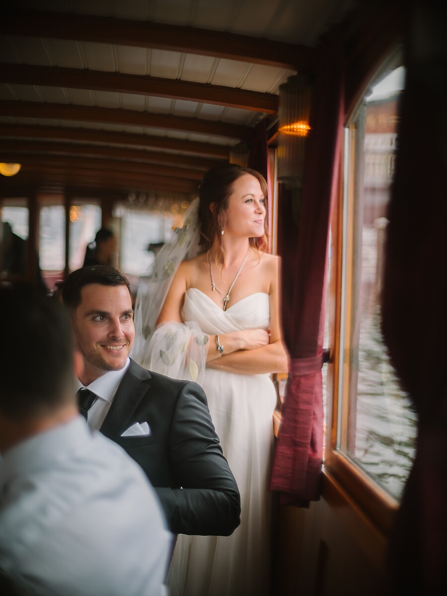 Wedding Ceremony SP6 Bruid in een jurk zonder bandjes kijkt uit het raam van een houten salonboot, een sessie op het water met een trouwfotograaf in Amsterdam