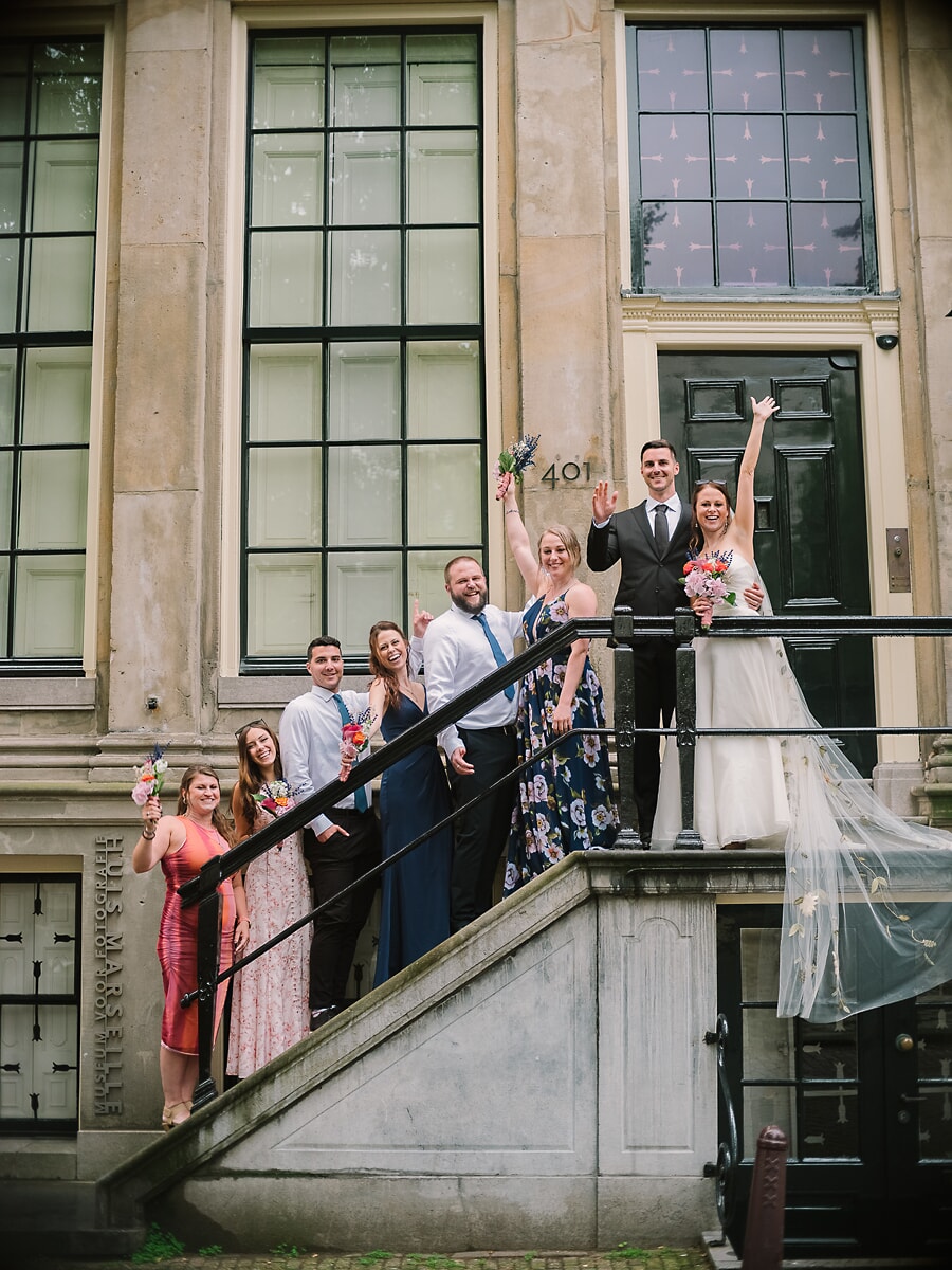 Wedding Ceremony SP8 Bruiloftsgezelschap juicht op de stoep van een historisch grachtenpand, een vrolijk groepsmoment van een trouwfotograaf in Amsterdam