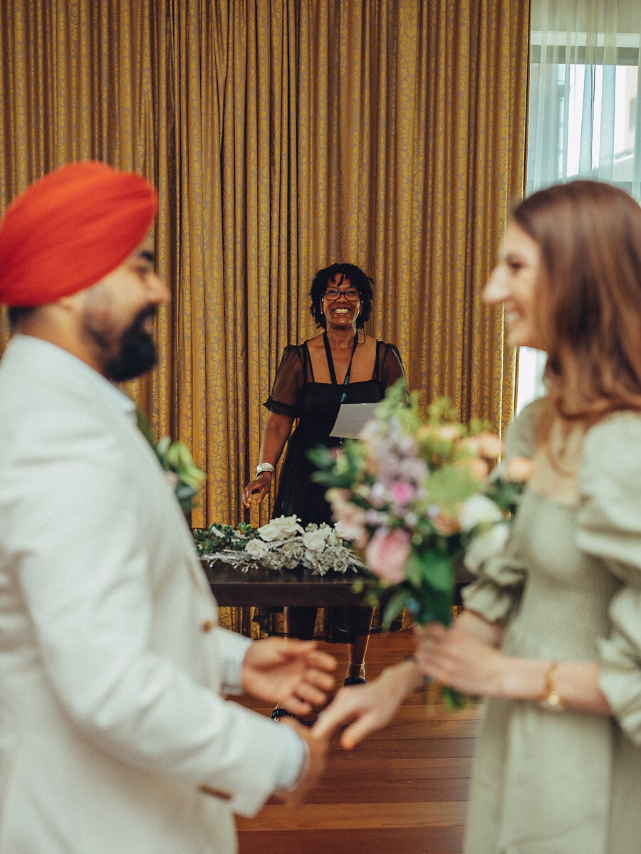 Wedding Ceremony SP9 Bruidegom in een crèmekleurig pak en rode tulband wisselt de ringen met zijn bruid voor de ceremoniespreker, vastgelegd in ongedwongen foto's van het burgerlijk huwelijk