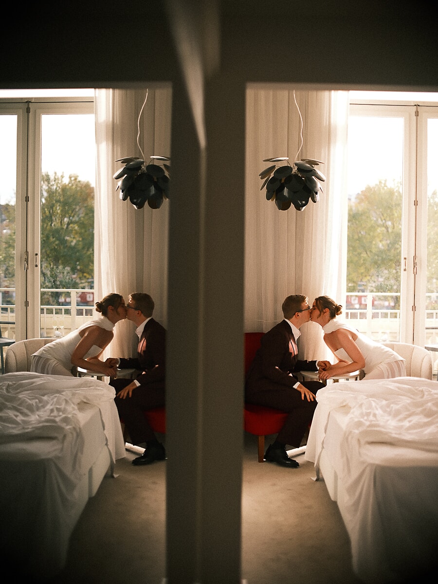Wedding Bridal SP1 Stel kust op een rode bank in een zonnige kamer, hun moment verdubbeld in de spiegel, door een trouwfotograaf in Amsterdam