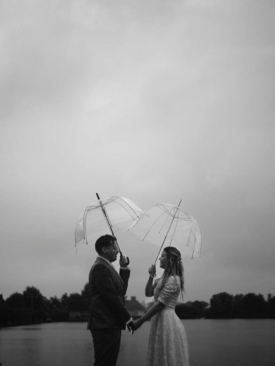 Wedding Bridal SP18 Zwart-witportret van een stel hand in hand onder twee doorzichtige paraplu's bij mistig water, door een trouwfotograaf in Amsterdam